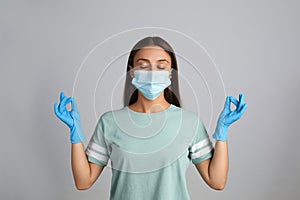 Woman in protective mask meditating on grey background. Dealing with stress caused by COVIDâ€‘19 pandemic