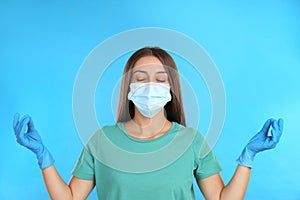 Woman in protective mask meditating on light blue background. Dealing with stress caused by COVIDâ€‘19 pandemic