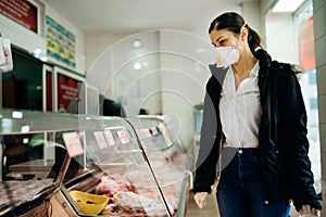 Woman with protective mask shopping for supplies.Budget shopping.Buying fresh meat at a butchery.Beef,pork,chicken infection.