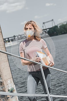 woman in protective mask standing on bridge with books air