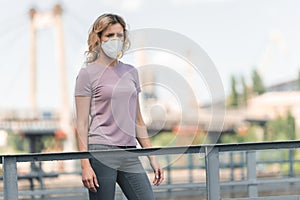 woman in protective mask standing on bridge and looking away air