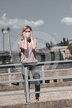 woman in protective mask standing on bridge and touching head air