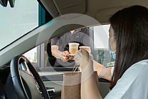 Woman in protective mask taking coffee at drive thru during covid-19 outbreak. photo