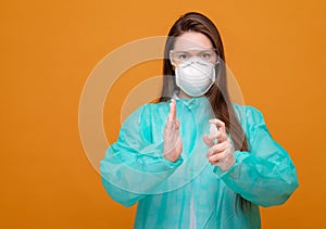 woman in protective medical equipment with antiseptic in hands medical mask on face on  yellow background, coronavirus pandemic