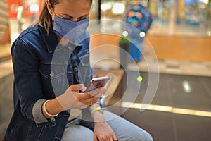 Woman in protective medical mask sits and holds smartphone in her hands.