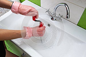 Woman in protective rubber gloves unblocking a clogged sink with a probe or drained cable at home.