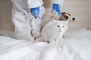 A woman in a protective suit is holding a dog and a cat