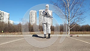 Woman in a protective suit, mask and gloves prepare to makes yoga exercises in empty city park.