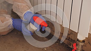 A woman in a protective suit and a respirator sprays a special antifungal spray on the mold-infested wall under the