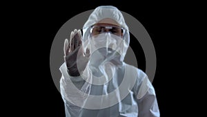 Woman in protective suit showing stop sign against dark background, caution