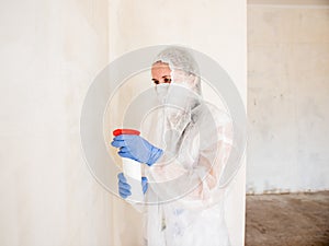 A woman in a protective suit sprays the walls of an apartment with a chemical agent to remove mold.