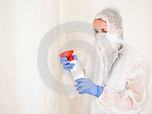 A woman in a protective suit sprays the walls of an apartment with a chemical agent to remove mold.