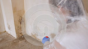 A woman in a protective suit, using a spray gun to spray the affected walls with mold.