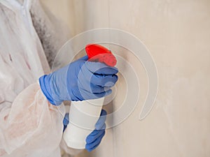 A woman in a protective suit, using a spray gun to spray the affected walls with mold.