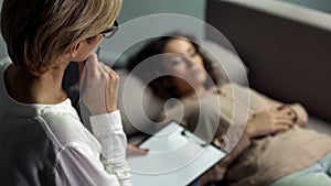 Woman psychologist listening to young lady lying on sofa during personal session