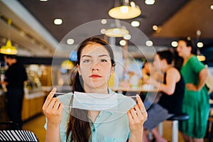 Woman in public place removing protective face mask.Safety measures and mask wearing in restaurants and cafe concept.Relief from