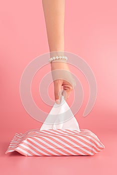 Woman pull the tissue paper out of the tissue box isolated on pink background, vertical. sanitation and hygiene facility concept.