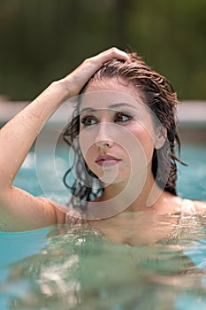 Woman pulling back her hair and glancing away from camera in the pool