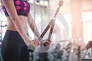 Woman pulling weight to train her arm and shoulder muscles in fitness gym