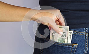 The woman pulls money out of the back pocket of the standing man`s blue jeans. Close-up view of the hands. Place for your text