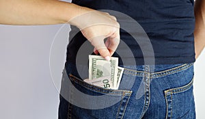 The woman pulls money out of the back pocket of the standing man`s blue jeans. Close-up view of the hands. Place for your text