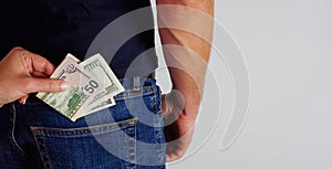 The woman pulls money out of the back pocket of the standing man`s blue jeans. Close-up view of the hands. Place for your text