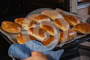 The woman pulls out ready-made Russian pies with filling from the oven. Homemade baking