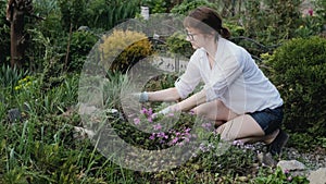 A woman pulls out weeds in a garden bed with her hands. Countryside. Summer weather. Manor.