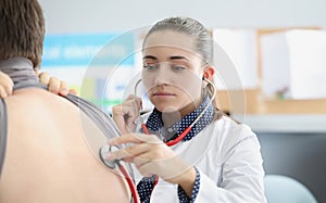 Woman pulmonologist listening to lungs of patient with stethoscope in clinic