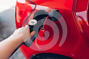 Woman pumping gas fuel into car at filling station. Petrol station customer holds nozzle refueling automobile.