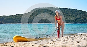 A woman pumps up a large yellow SUP board on the seashore and prepares for a walk on the sea. Active recreation