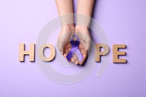 Woman with purple awareness ribbon and word HOPE made of wooden letters on violet background