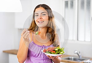 Woman in purple nightgown sits on a table and eats a vegetable salad in her kitchen