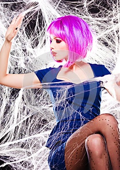 Woman with purple wig and intense make-up trapped in a spider web