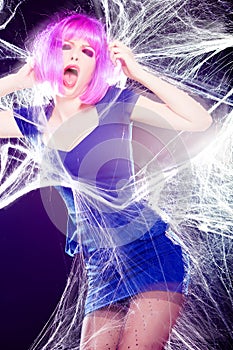 Woman with purple wig and intense make-up trapped in a spider web screaming