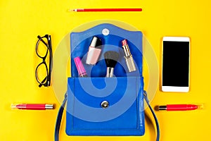 Woman purse, beauty products, smartphone, glasses on a bright yellow background, top view