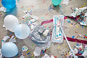 Woman with pushbroom cleaning mess of floor in room after party confetti