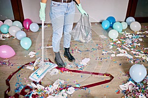 Woman with pushbroom cleaning mess of floor in room after party confetti