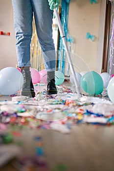 Woman with pushbroom cleaning mess of floor in room after party confetti