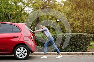 Woman pushing broken car on the road