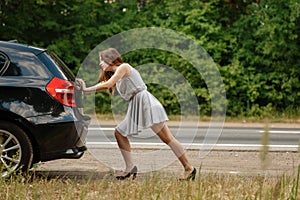 Woman pushing broken car on road, breakdown