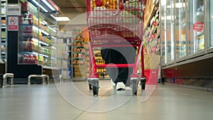 Woman pushing a cart in a supermarket store in slow motion, close-up shot from a low angle. Grocery shopping concept