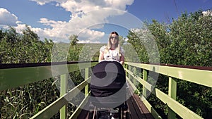 Woman pushing her baby in a pram over a narrow foot bridge