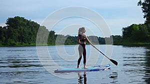 Woman pushing and pulling the paddle through shining water surface and propelling paddleboard on sunny morning