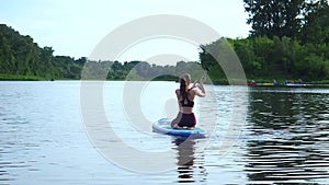 Woman pushing and pulling the paddle through shining water surface and propelling paddleboard on sunny morning
