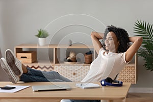 Woman put hands behind head legs on desk relaxing indoors