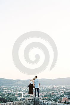 Woman put her head on the man shoulder on a stone wall overlooking the mountains. Back view