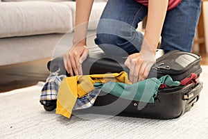 Woman Put Her Weight on Her Knees on Overfilled suitcase, in order to Fit All Her Clothes in to It