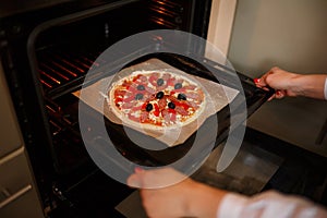 Woman put Raw pizza with ingredients and tomato, spices, sausages on baking tray