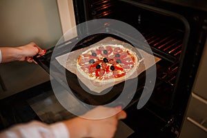 Woman put Raw pizza with ingredients and tomato, spices, sausage